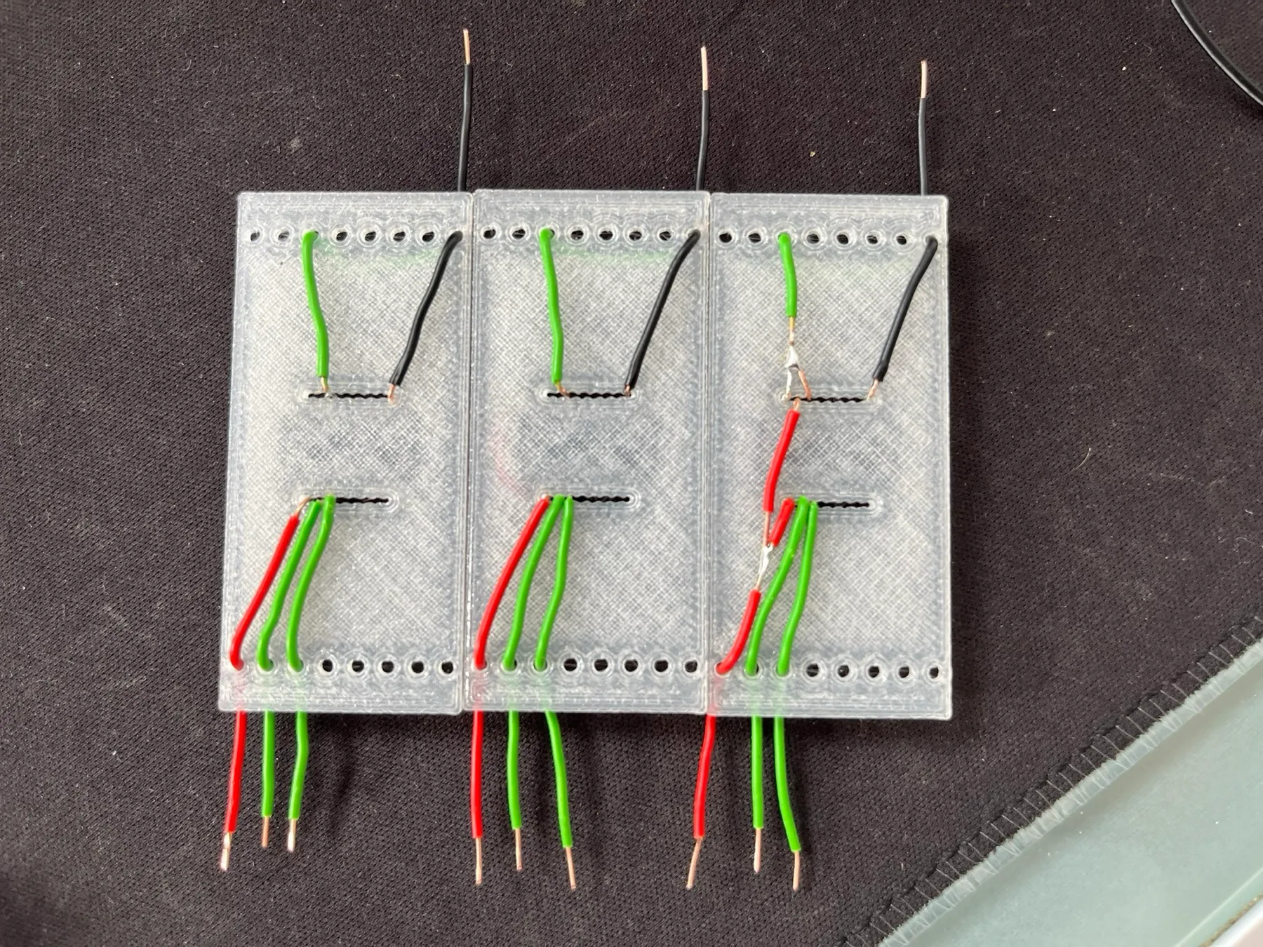 Back side of three clear 3D-printed carrier boards with red, green and black wires routed through slots.