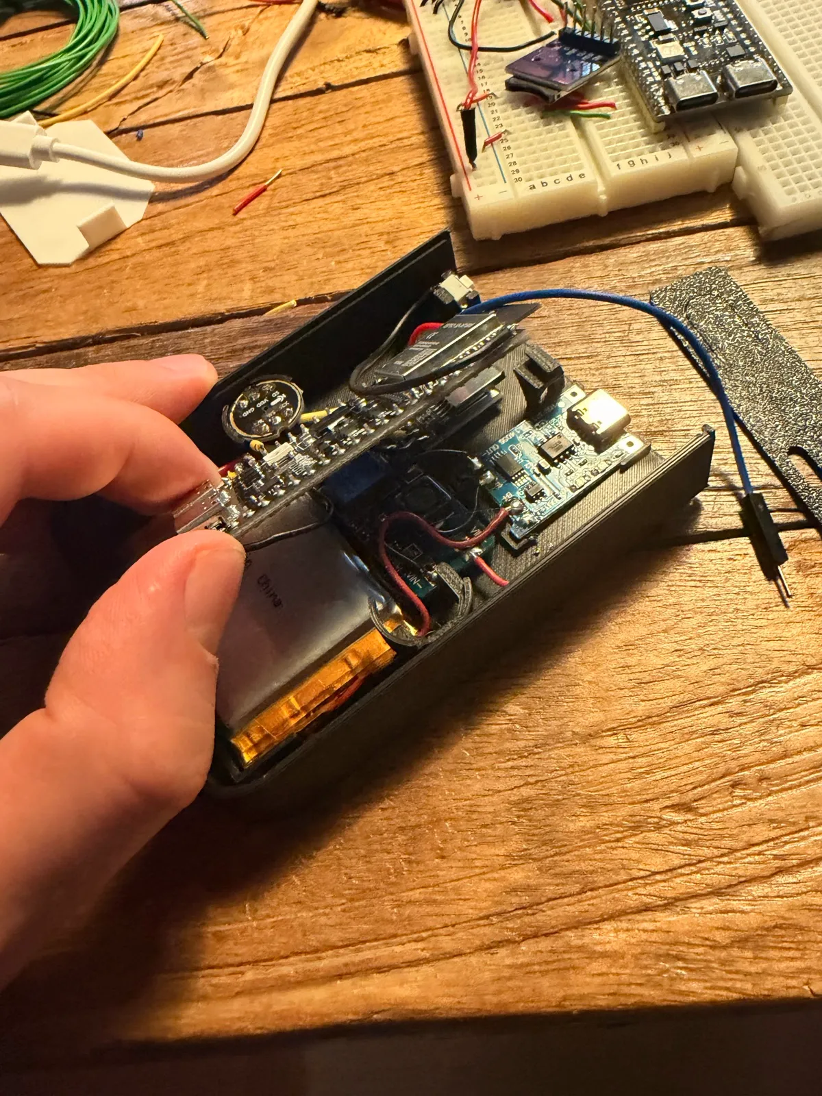 A hand lowering the ESP32 board into the V1 shell over the battery and power boards.
