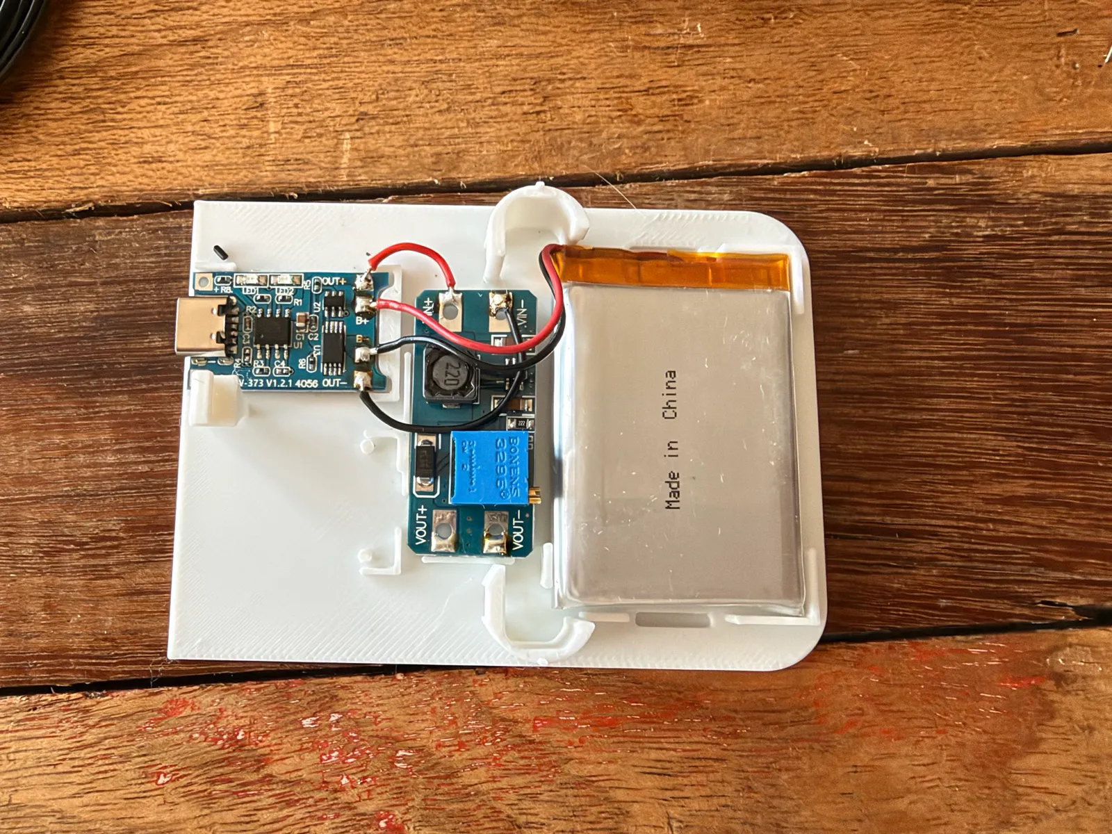 The first print of the V1 shell, its white base plate holding a USB-C charging board, a boost converter and a flat LiPo battery.