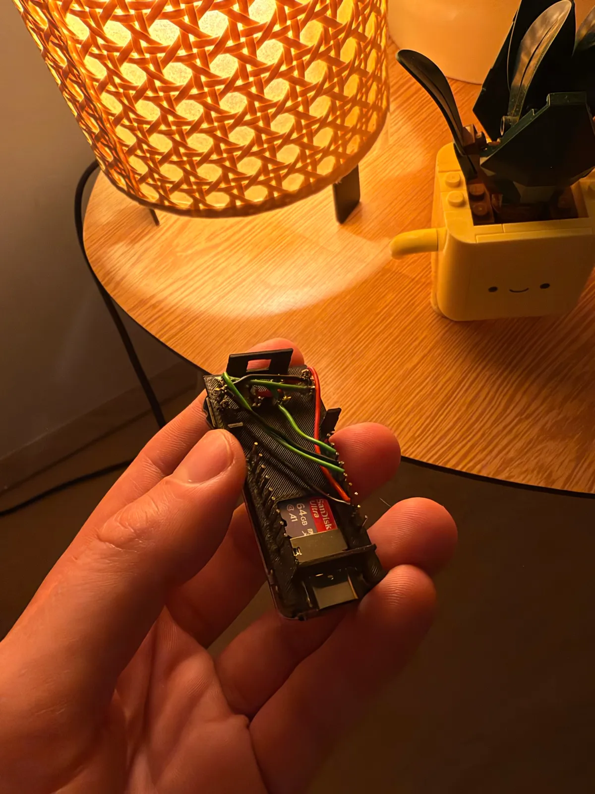 The V2 board held in a hand inside its printed frame, wires running across it and a microSD card in the slot.