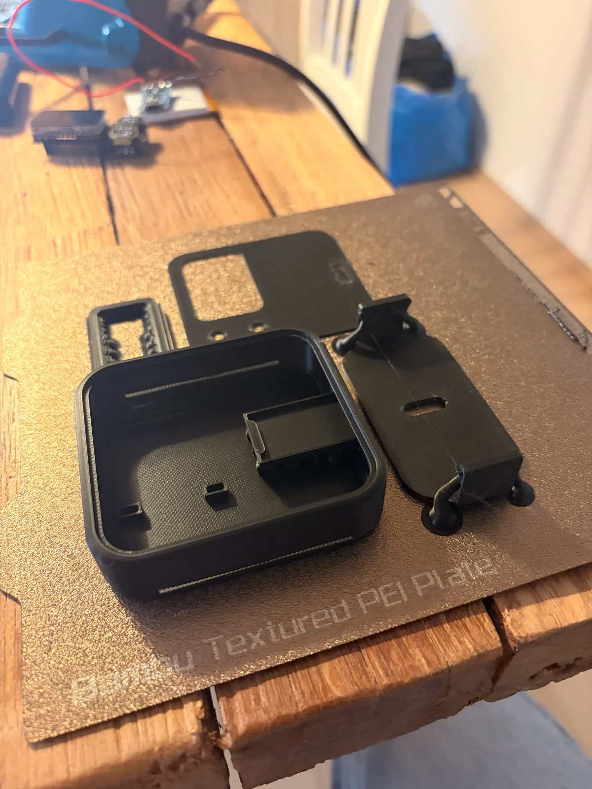 The V2 parts fresh off a textured print bed: the rounded-square body, the sliding cover with its keyhole slot, and the inner frame.
